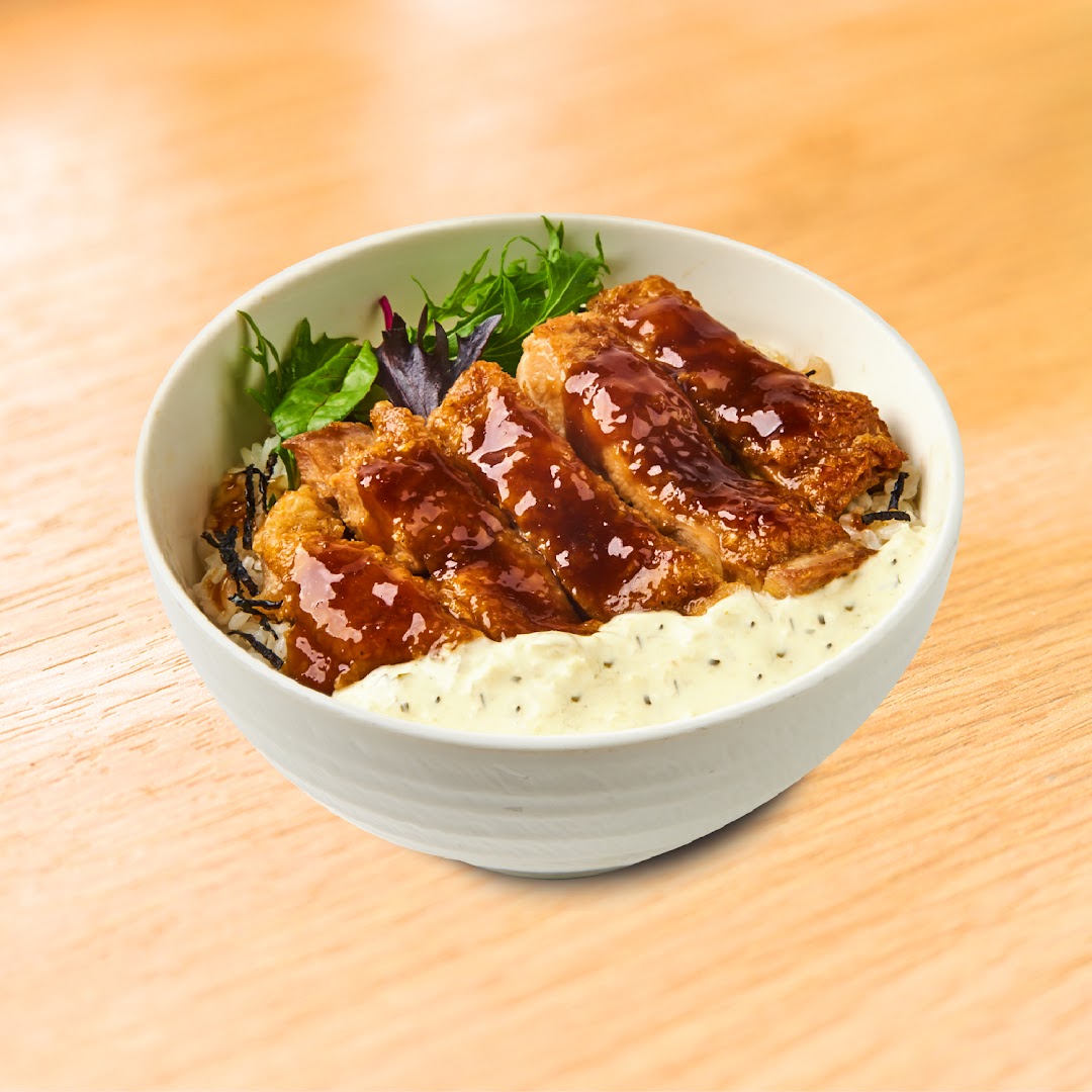Close-up of a bowl of chicken teriyaki with rice, sauce, and greens.