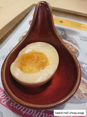 A half-cut soft-boiled egg with a runny yolk in a small red dish.