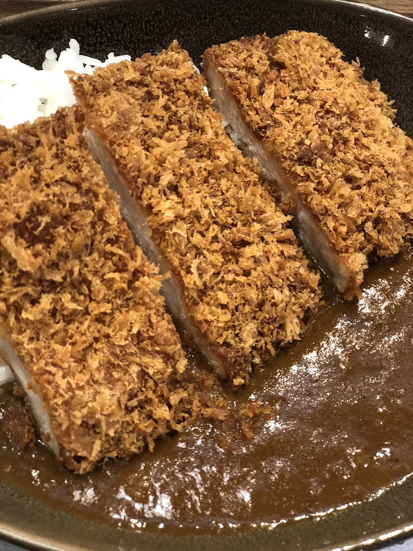 A close-up of tonkatsu curry with rice in a bowl.