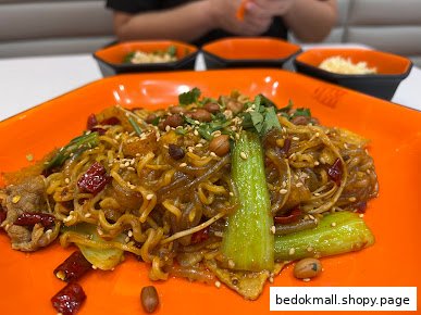 A close-up of a spicy noodle dish with peanuts and vegetables on an orange plate.