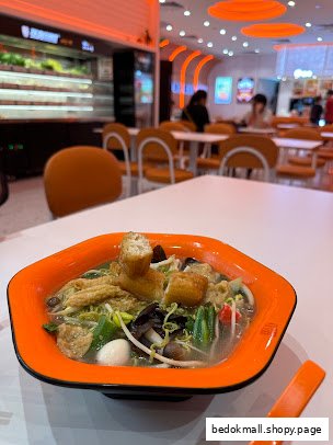 A bowl of Mala Tang on a table in a brightly lit restaurant interior.