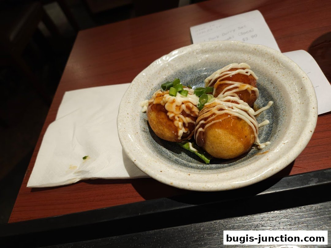 A bowl of takoyaki drizzled with sauce and mayonnaise, garnished with green onions.