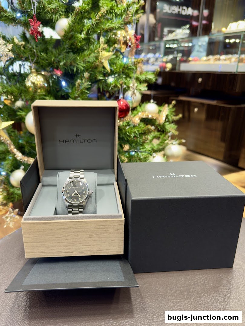 A Hamilton watch displayed in its box with a festive Christmas tree in the background.