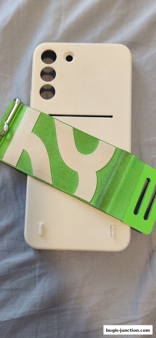 A white smartphone with a green strap featuring a white pattern lies on a grey fabric surface.