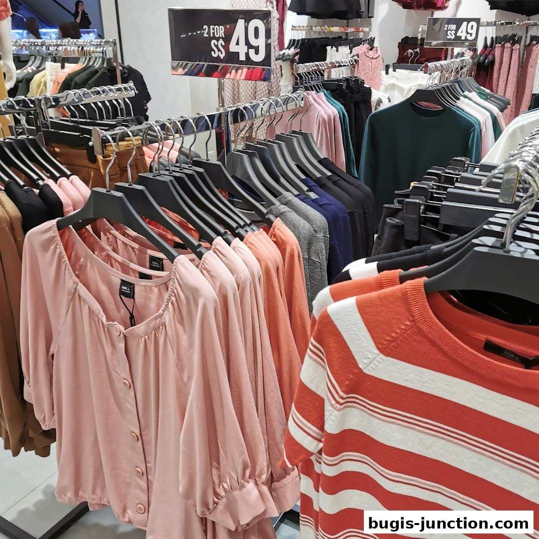 A display of women's clothing, featuring pink blouses and striped tops, with a sale sign.