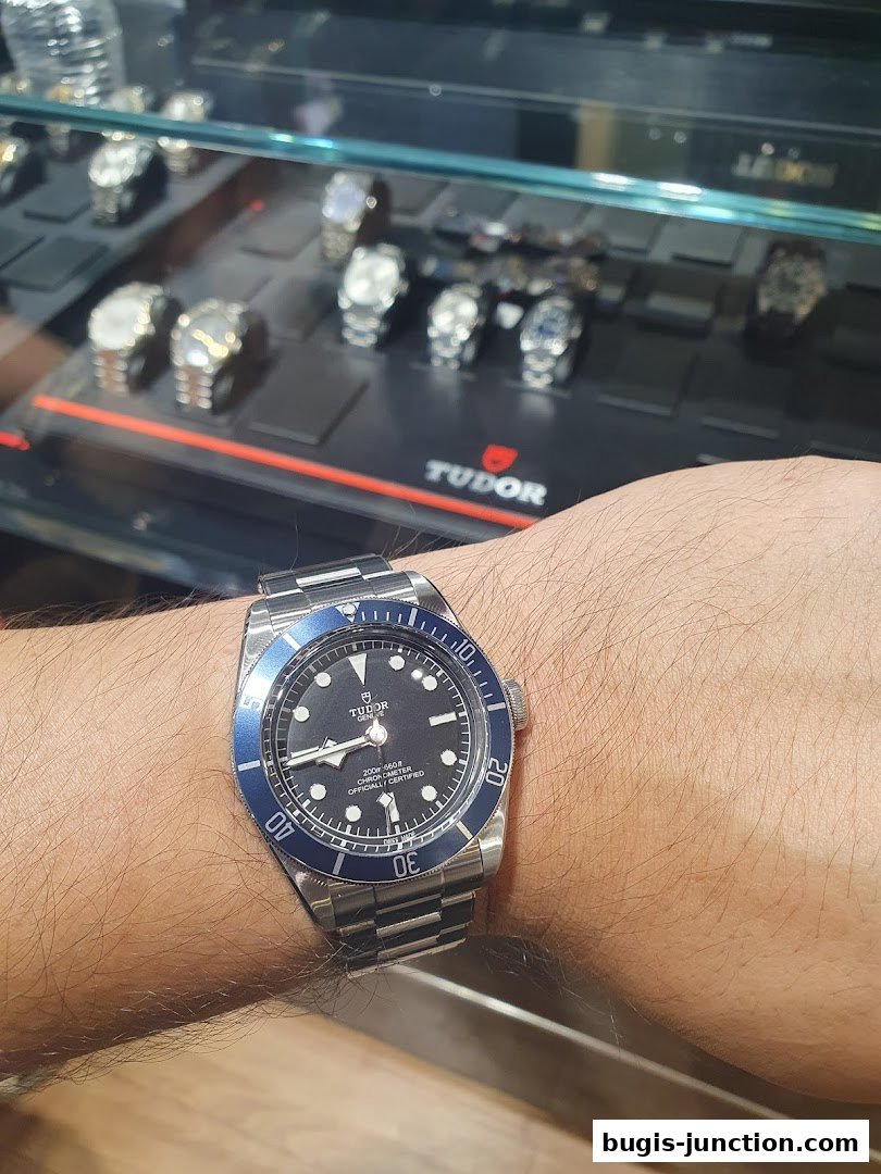 A person wearing a Tudor watch in front of a display of watches.
