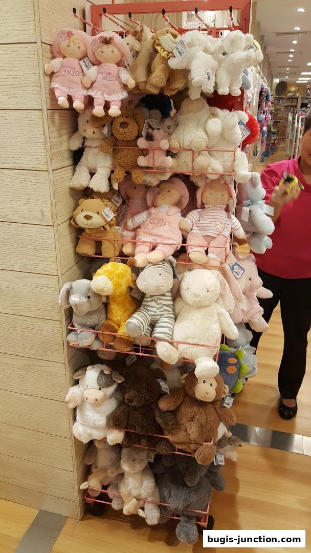 A display rack filled with various soft plush toys, including dolls, animals, and teddy bears.