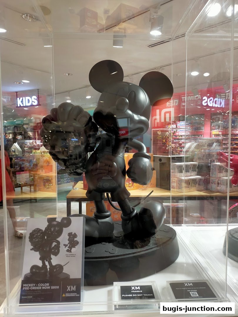 A large black Mickey Mouse statue is displayed in a glass case, with a price tag and store information visible.