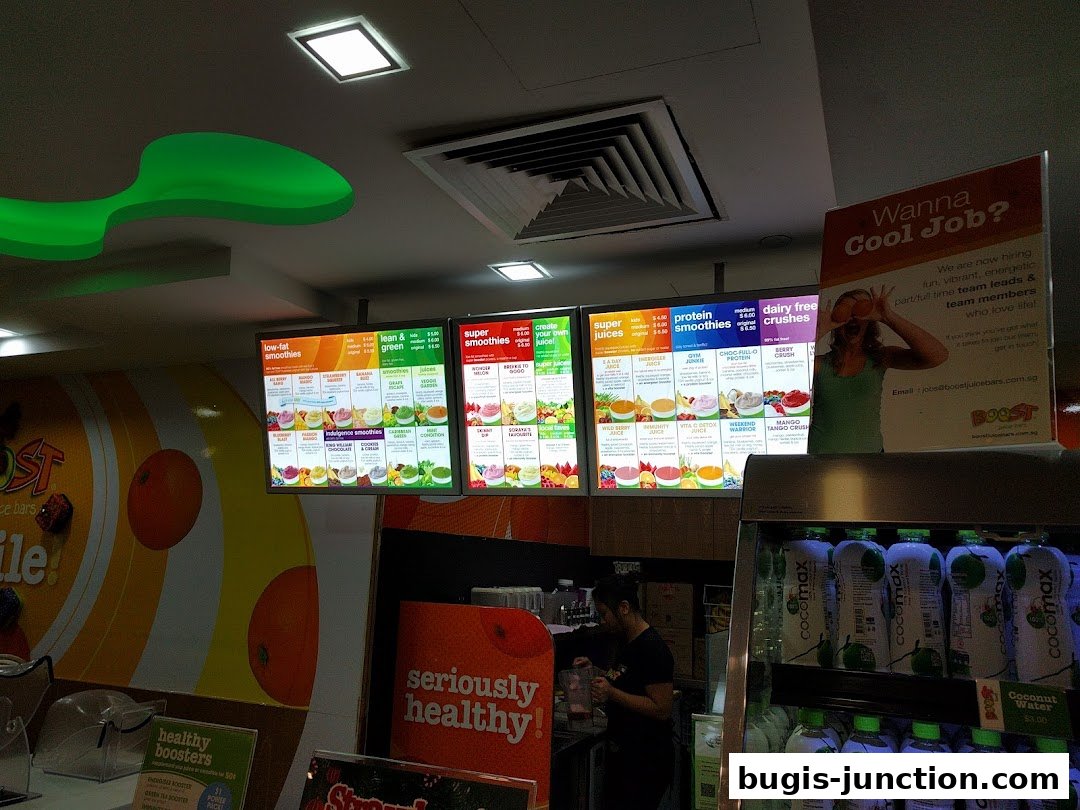 A Boost Juice shop interior with illuminated menus displaying smoothies and juices, and a hiring poster.