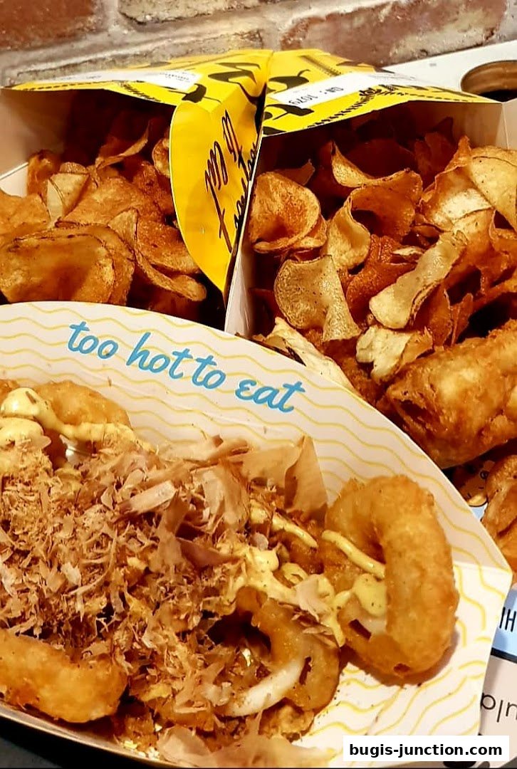 Close-up of crispy fried fish and chips with toppings and potato chips.
