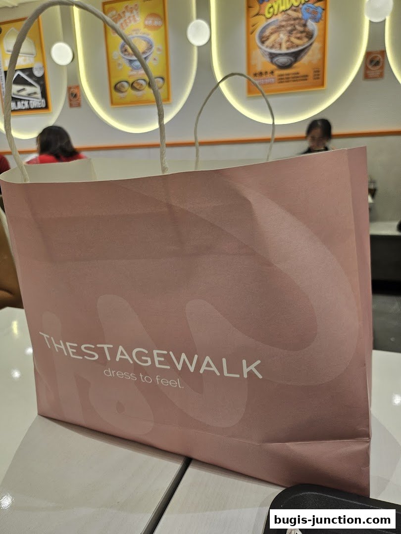 A pink shopping bag with 'THESTAGEWALK' logo and slogan 'dress to feel.'