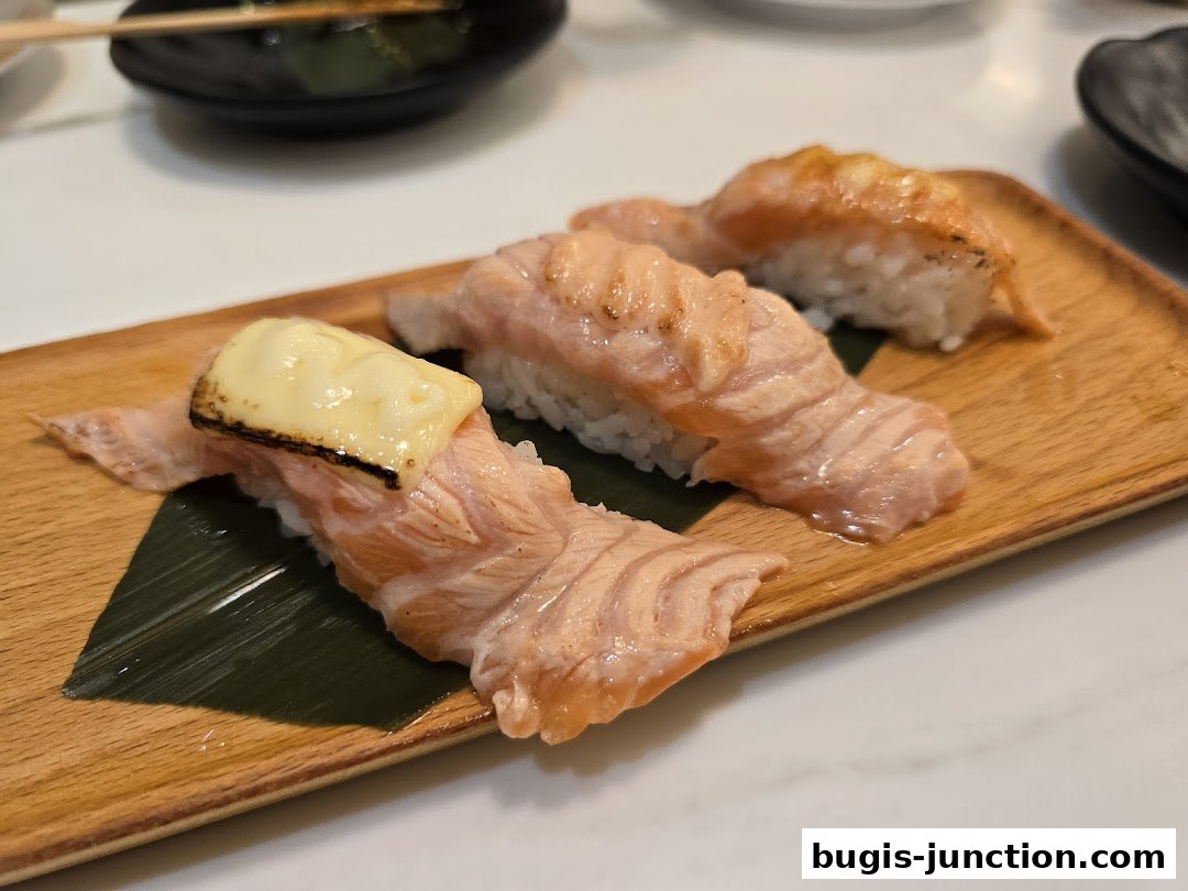Close-up of three pieces of salmon sushi with cheese topping on a wooden plate.