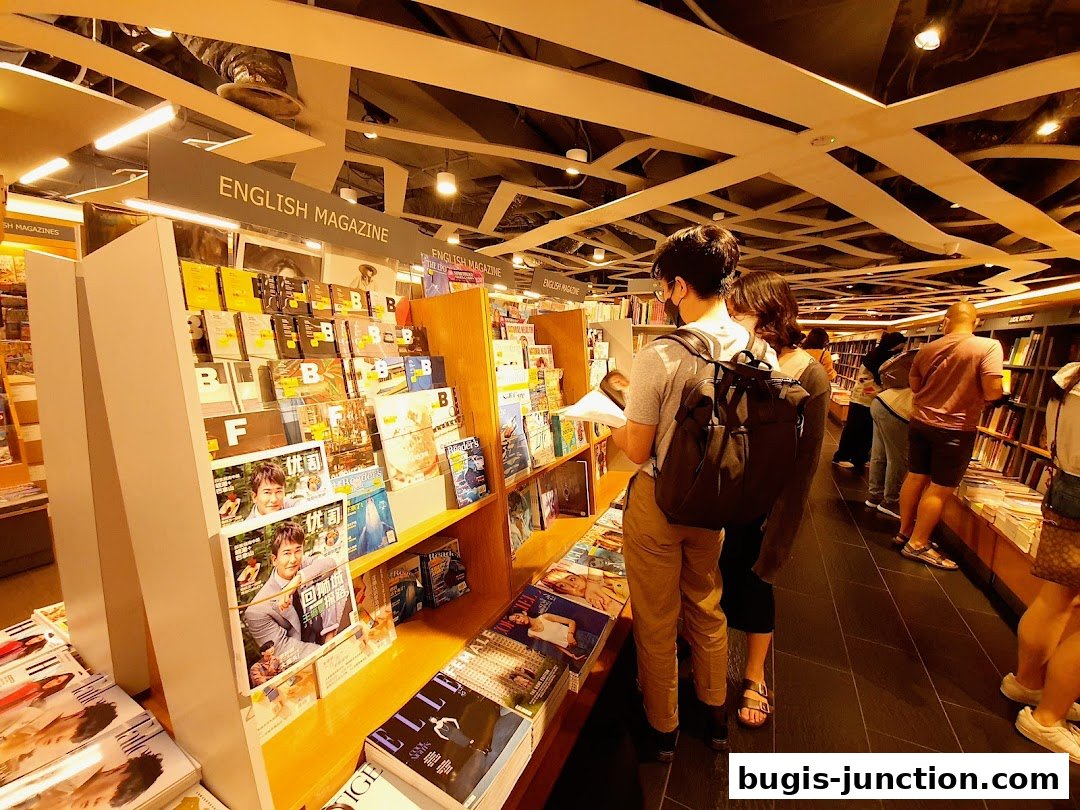 Customers browse magazines and books in a well-lit bookstore with modern ceiling design.