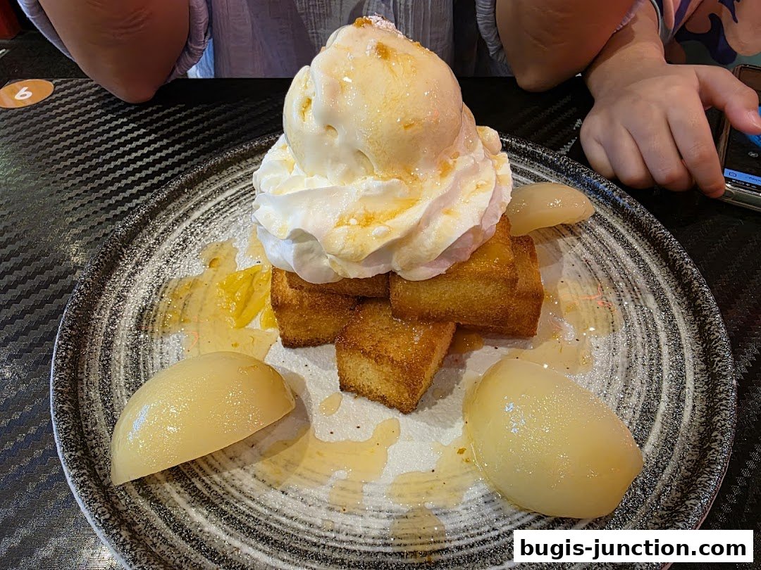 A dessert with ice cream, whipped cream, toast cubes, and pear slices on a plate.