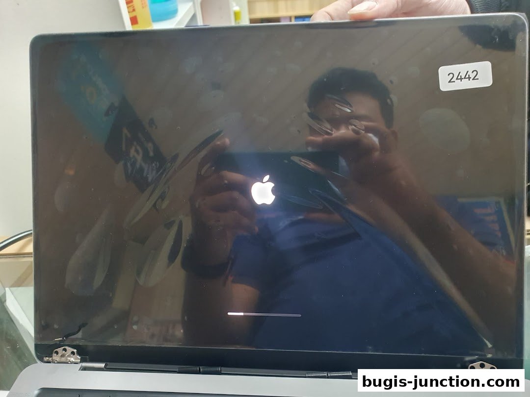 A person holds up a laptop screen displaying the Apple logo and a loading bar.