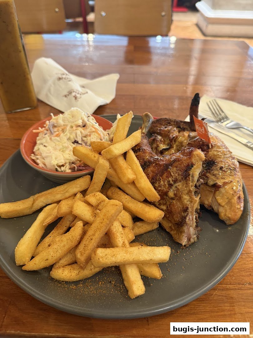 A plate of flame-grilled chicken with fries and coleslaw, served with a bottle of sauce.