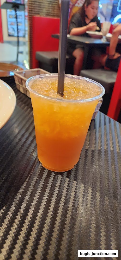 A close-up of a refreshing orange iced drink with a straw in a clear plastic cup.