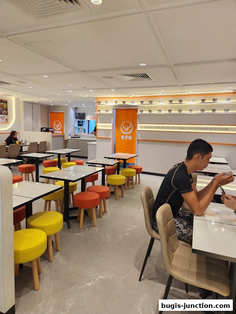Interior of Yoshinoya restaurant with tables, chairs, and customers dining.