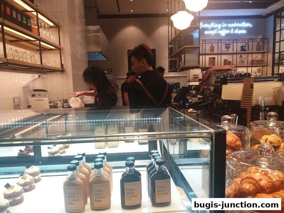 Interior of a cafe with pastries, cold brew coffee bottles, and a barista preparing drinks.