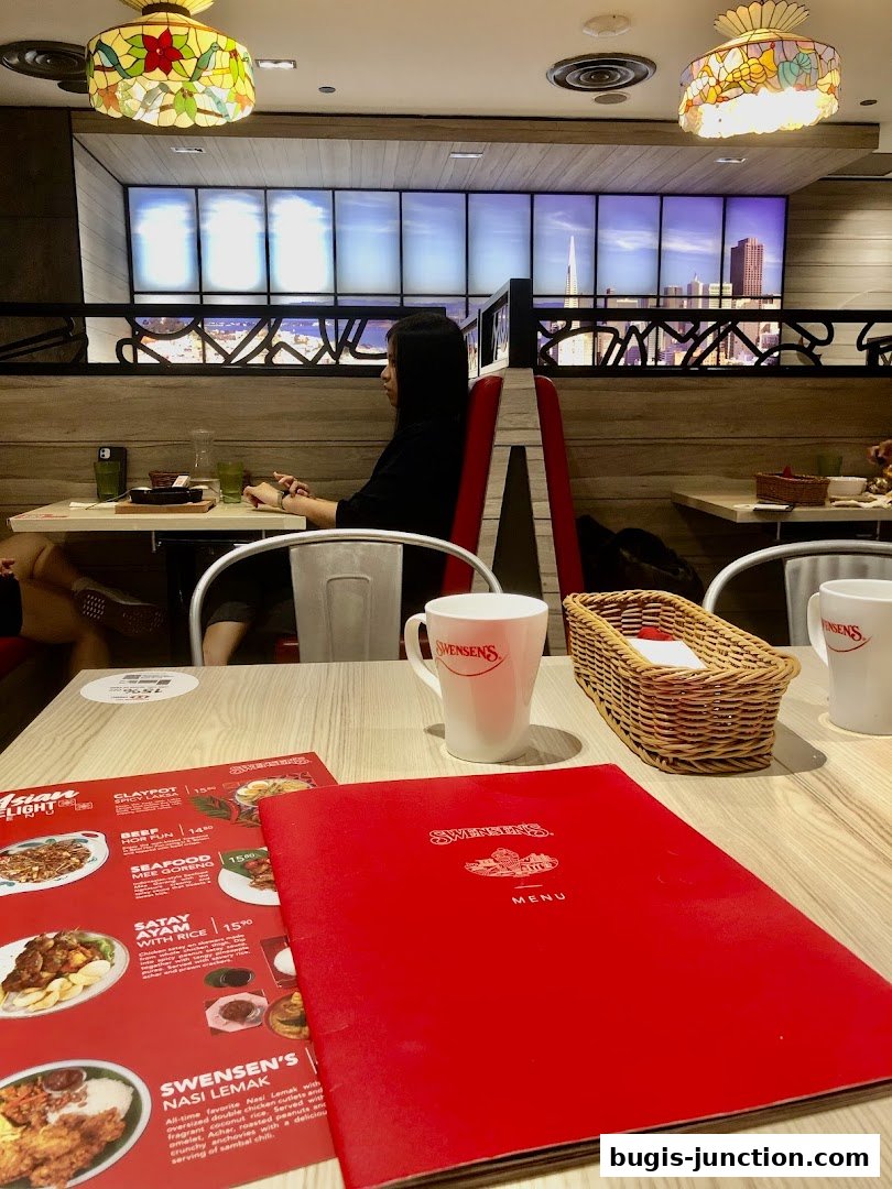 A table at Swensen's with menus, mugs, and a basket, with a person seated in the background.