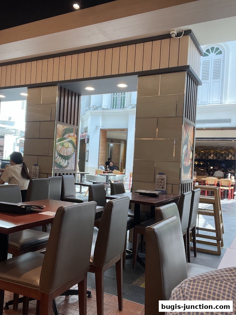 Interior view of Ajisen Ramen restaurant with tables and chairs, showing a glimpse of the mall walkway.