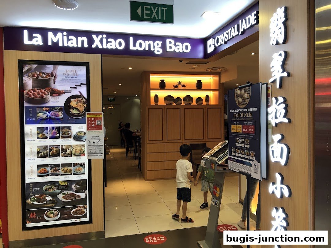 The entrance of Crystal Jade La Mian Xiao Long Bao restaurant with a digital menu display.
