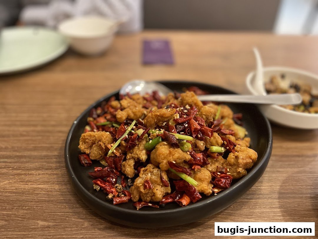A close-up of a spicy fried chicken dish with dried chilies and scallions on a black plate.