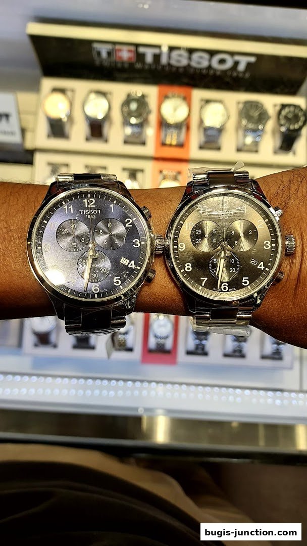 Two Tissot watches displayed on a wrist with a Tissot logo and watch display in the background.