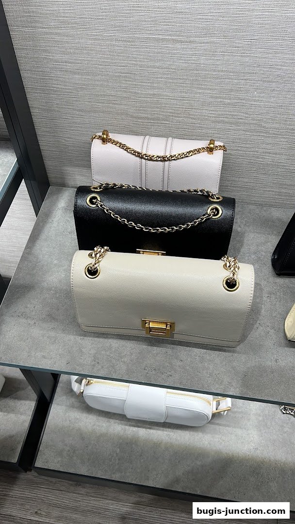 Three stylish chain-strap shoulder bags in light pink, black, and cream displayed on shelves.