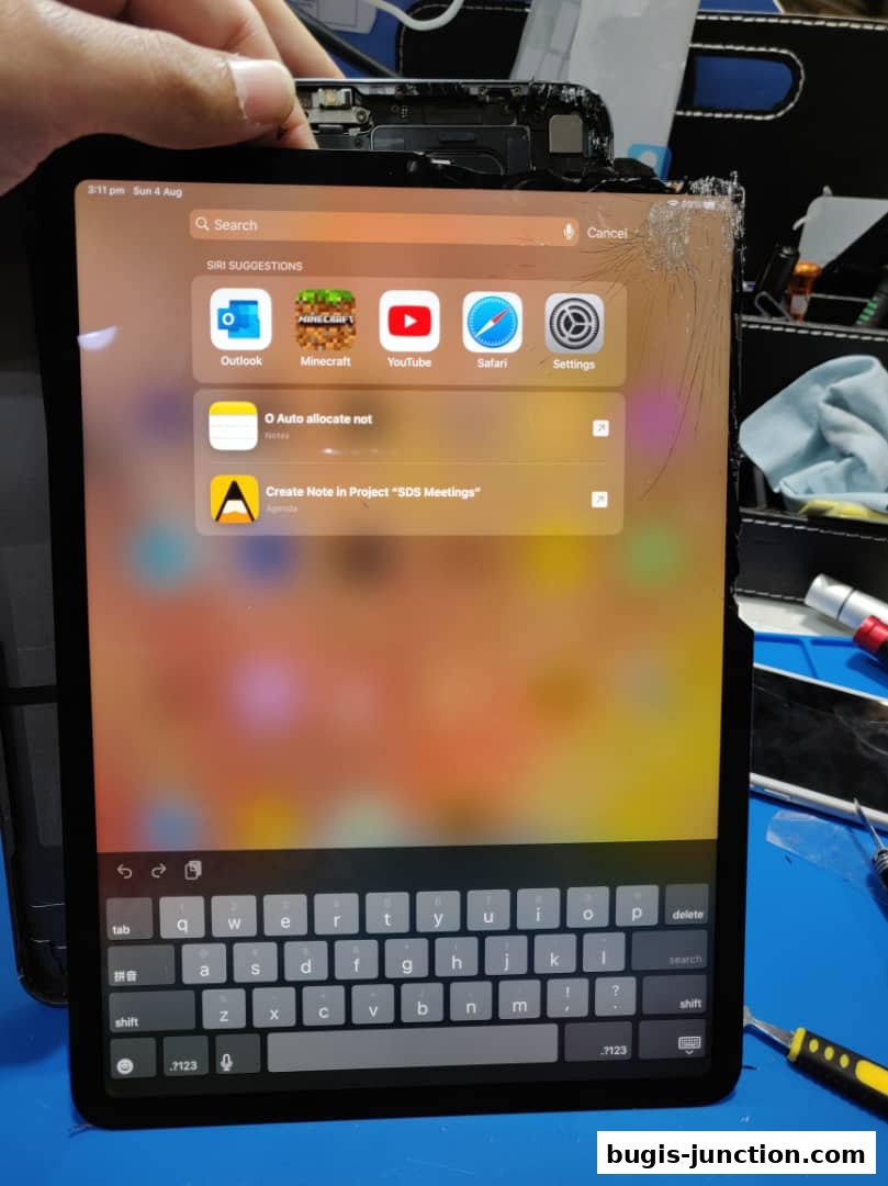 A cracked tablet screen displaying app icons and a keyboard, held by a hand.