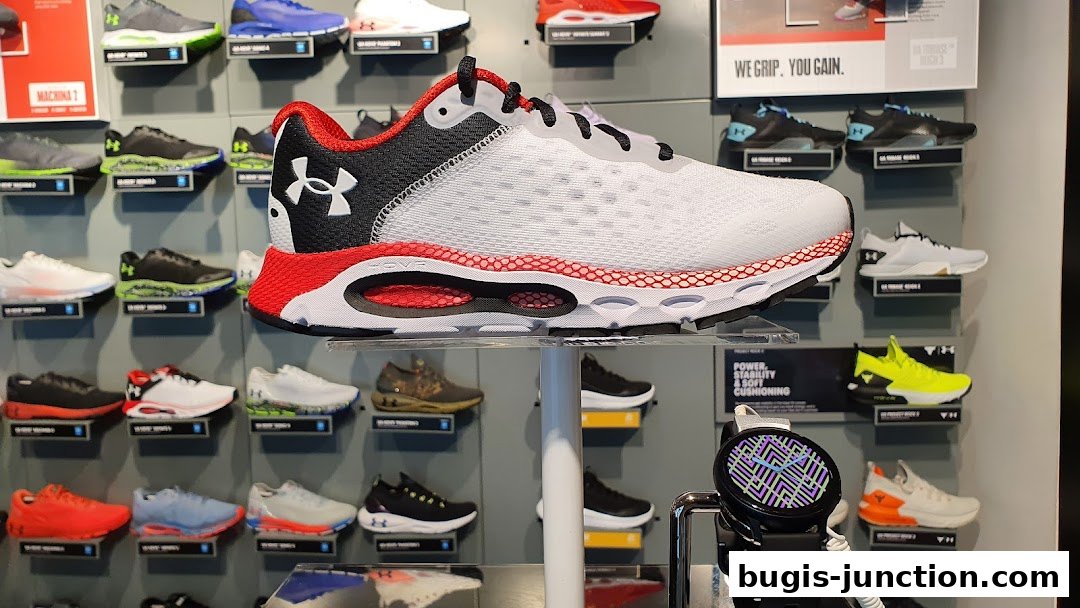 A display of various Under Armour running shoes, with a focus on a white and red model.