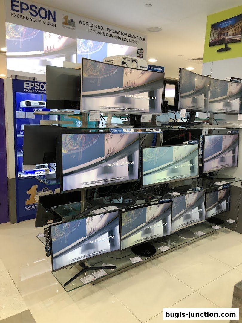 A retail store display featuring multiple Samsung curved monitors and Epson projectors.