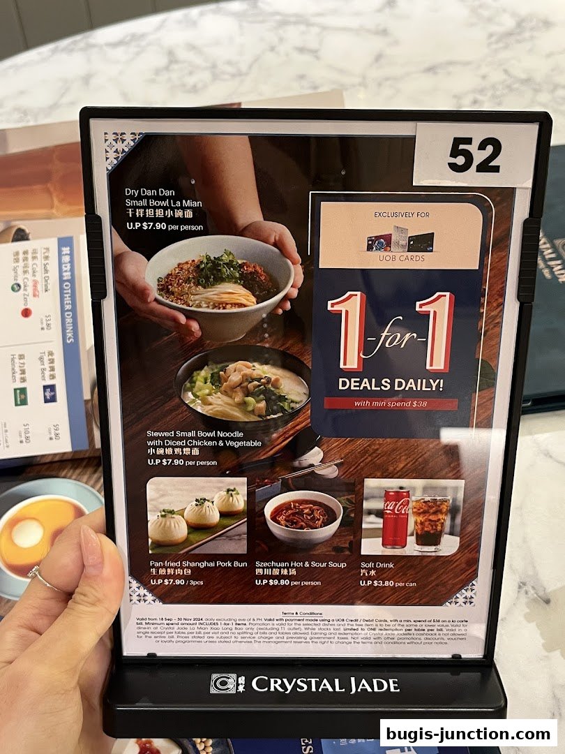 A menu board from Crystal Jade La Mian Xiao Long Bao featuring noodle dishes, buns, soup, and drinks.