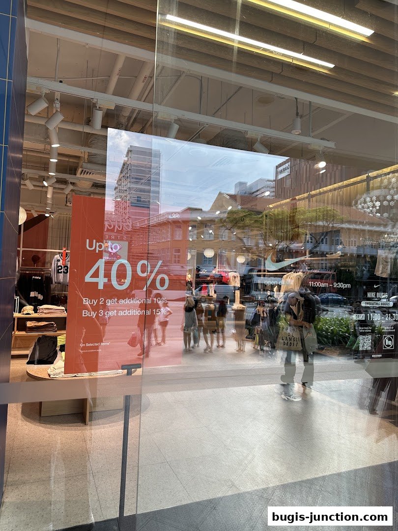 Nike store window display with a sale sign and reflections of people and buildings.