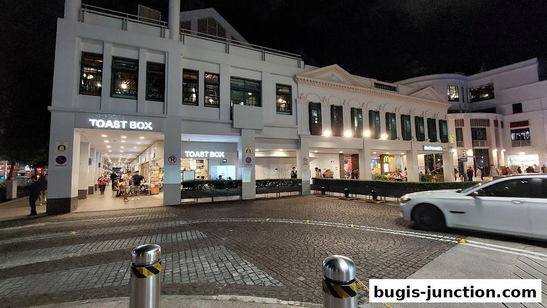 The exterior of Toast Box and McDonald's at night, with people walking by.
