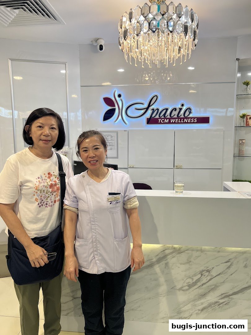 Two women stand in front of the Spacio TCM Wellness reception desk.