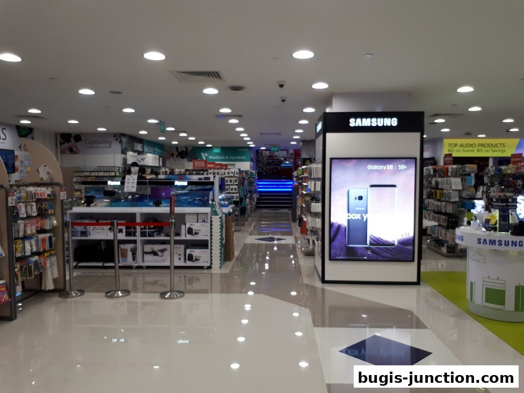 Interior view of a brightly lit electronics store with displays of phones, audio products, and accessories.