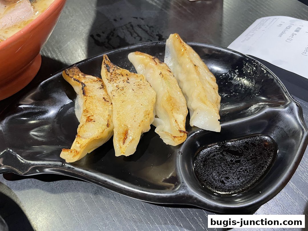 A plate of pan-fried gyoza with dipping sauce next to a bowl of ramen.