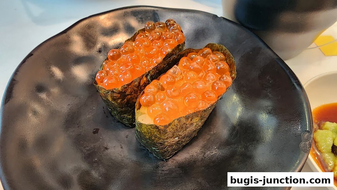 Two pieces of ikura gunkan maki sushi served on a black plate with soy sauce and wasabi.