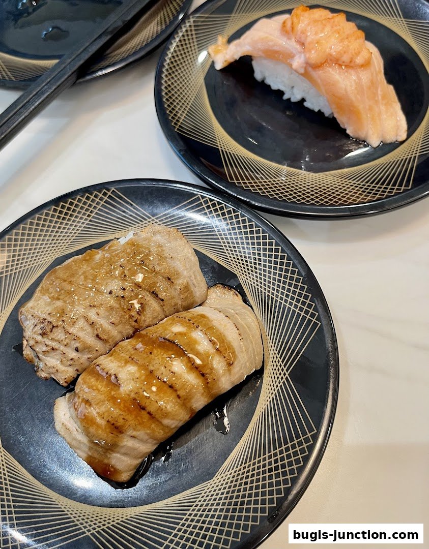 Two plates of sushi, one with grilled fish and another with salmon, are displayed on a white surface.