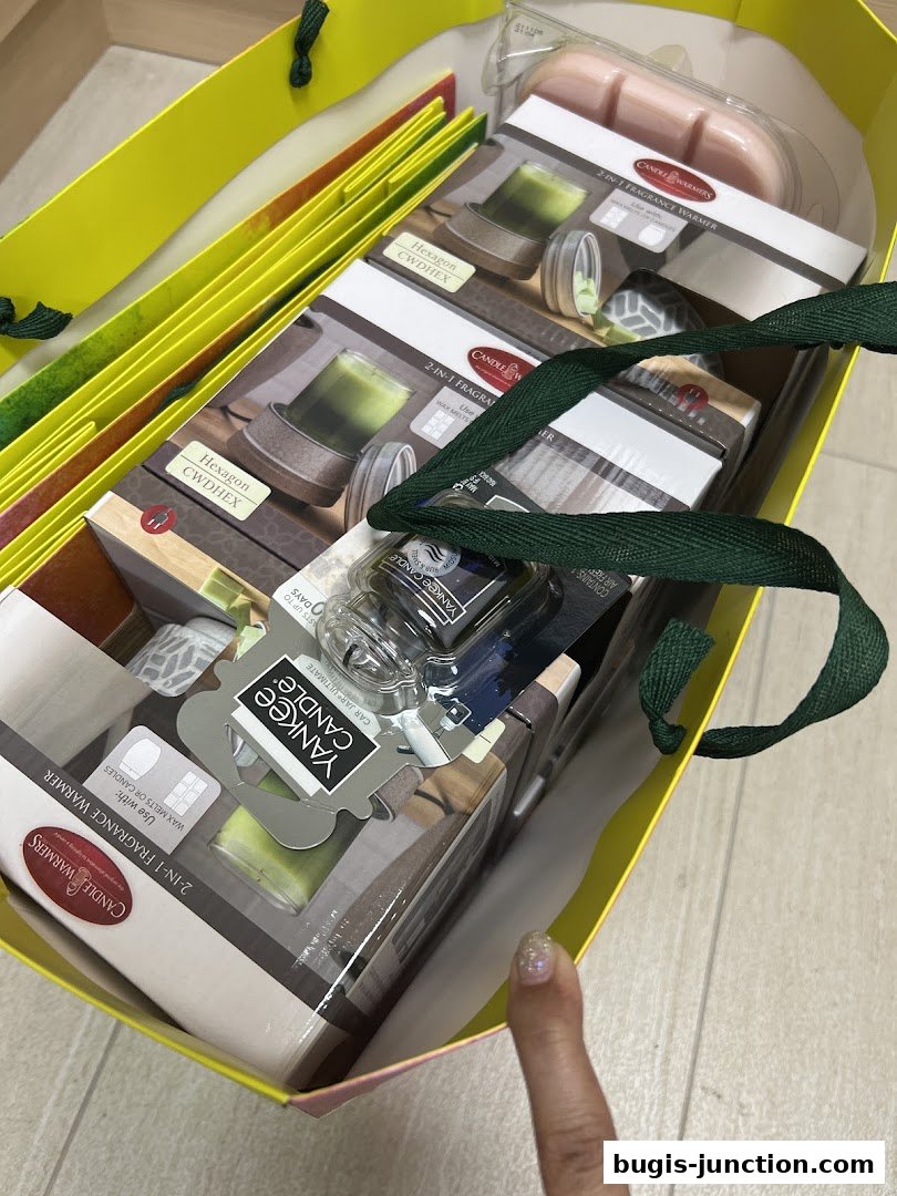 A yellow shopping bag filled with Yankee Candle products, including fragrance warmers and car air fresheners.