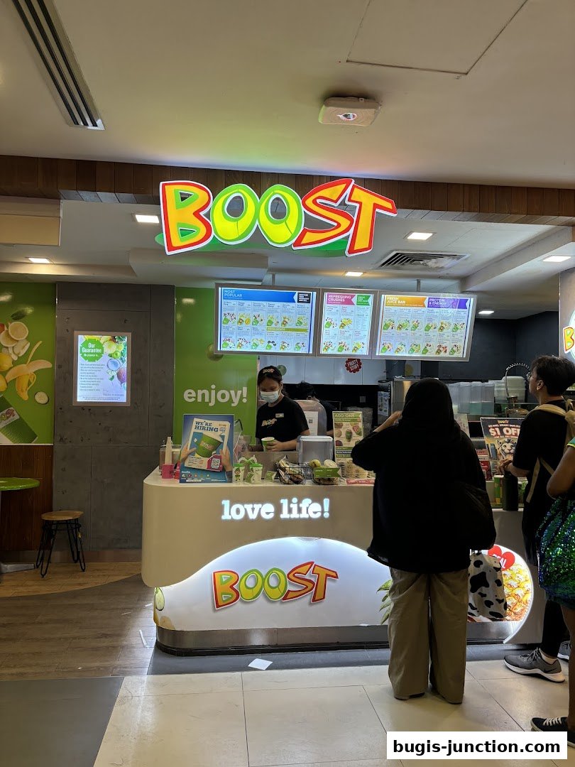 A Boost Juice shop with a bright sign, menu boards, and customers ordering.