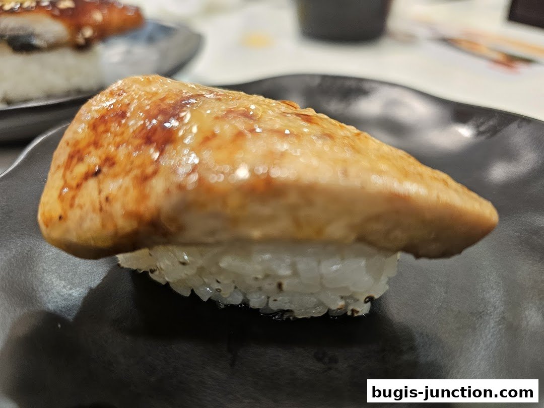 A close-up shot of a piece of sushi with grilled topping on a black plate.