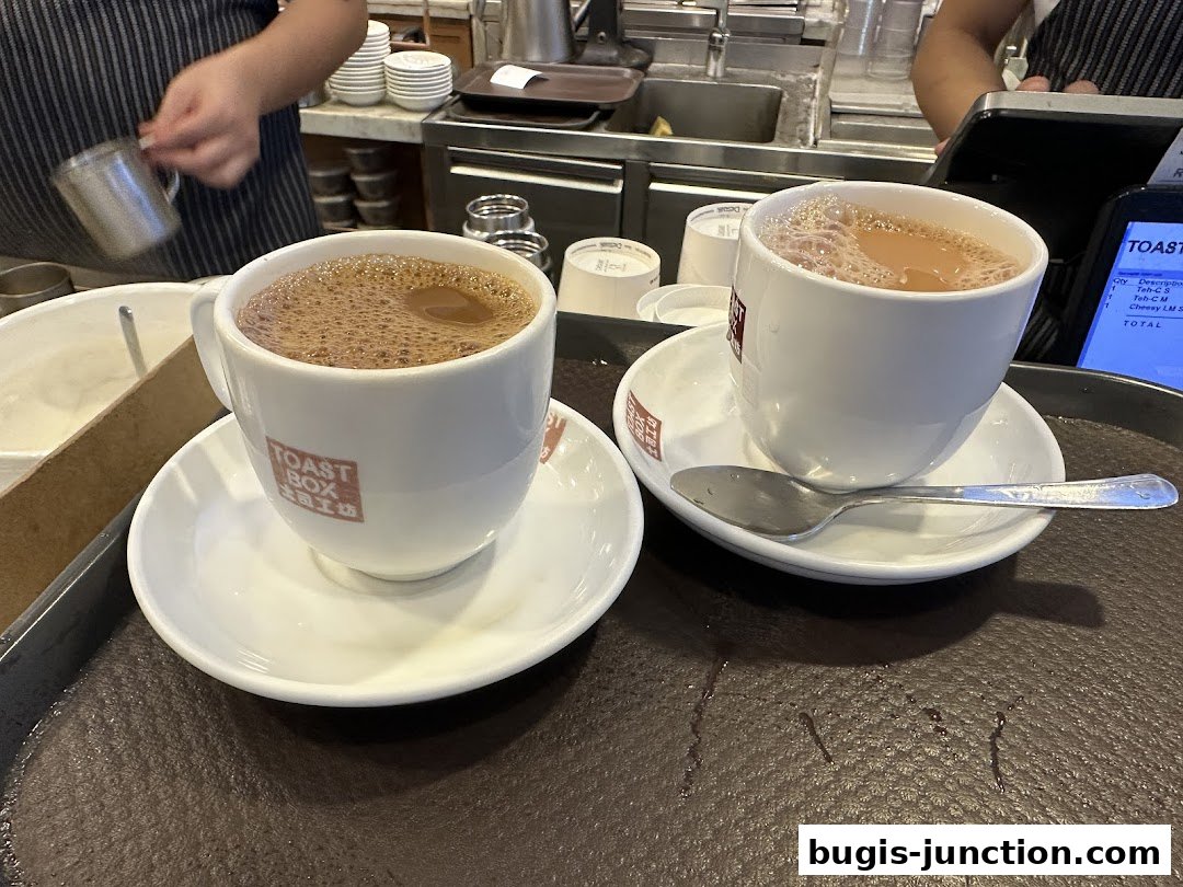 Two cups of frothy coffee on saucers with spoons on a tray.