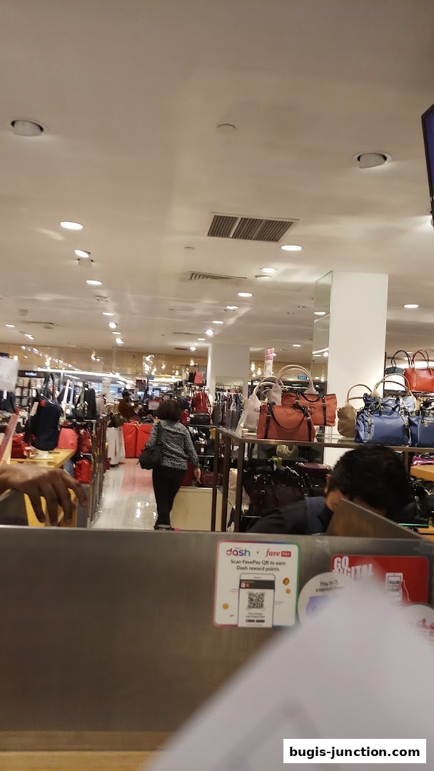 Interior view of a department store with handbags and clothing displays, and shoppers.