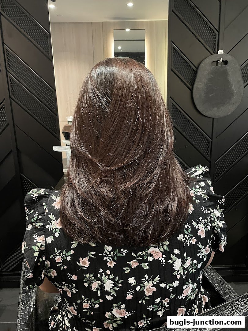 A person with beautifully layered brown hair sits in a salon chair, showcasing a fresh hairstyle.