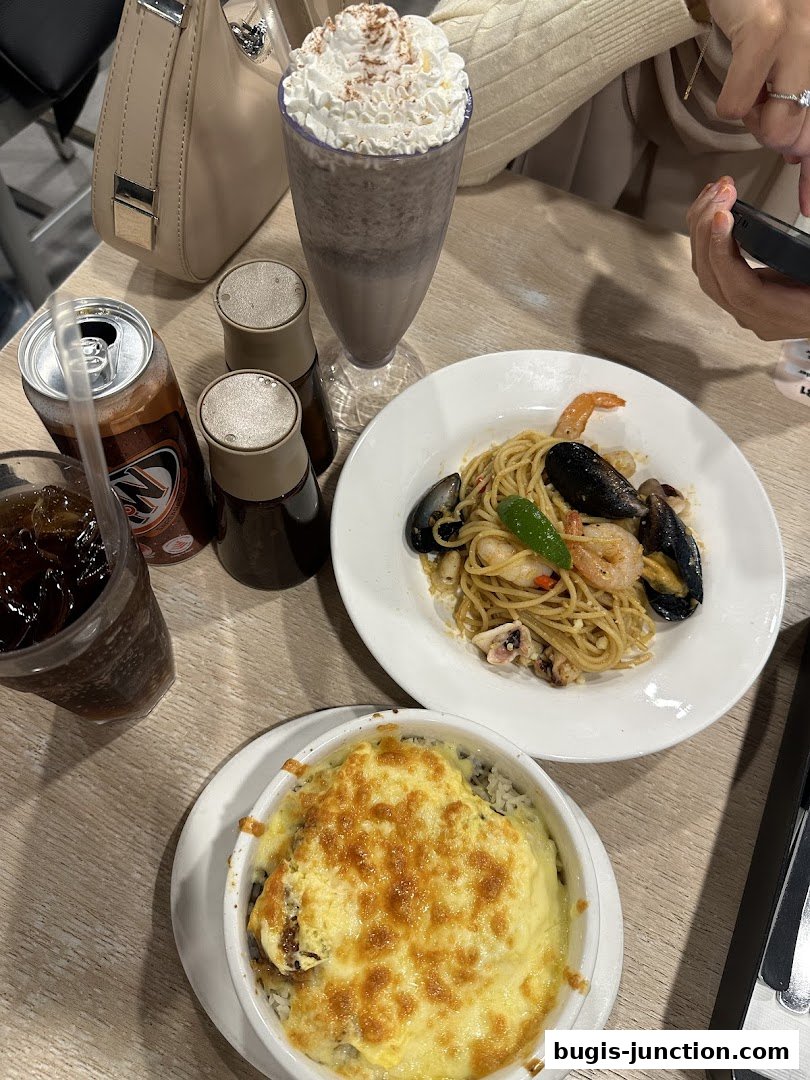 A table laden with delicious food, including pasta, baked rice, a milkshake, and drinks.