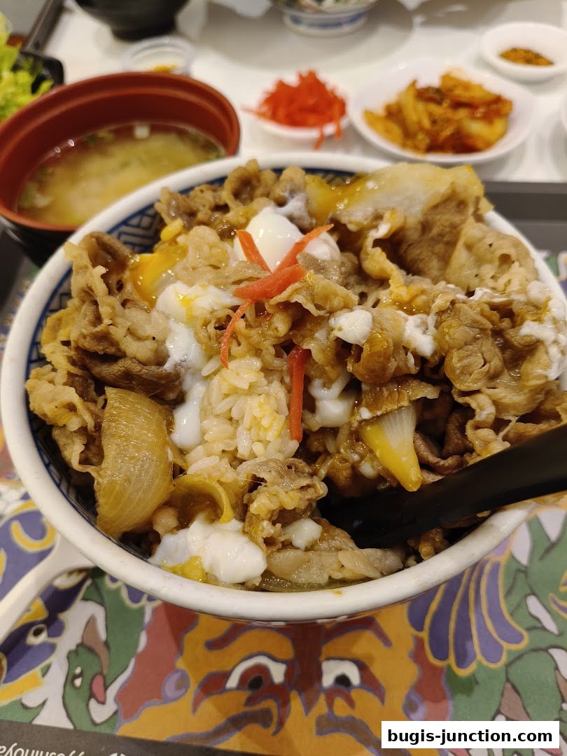 A close-up of a Yoshinoya beef bowl with rice, meat, egg, and pickled ginger.
