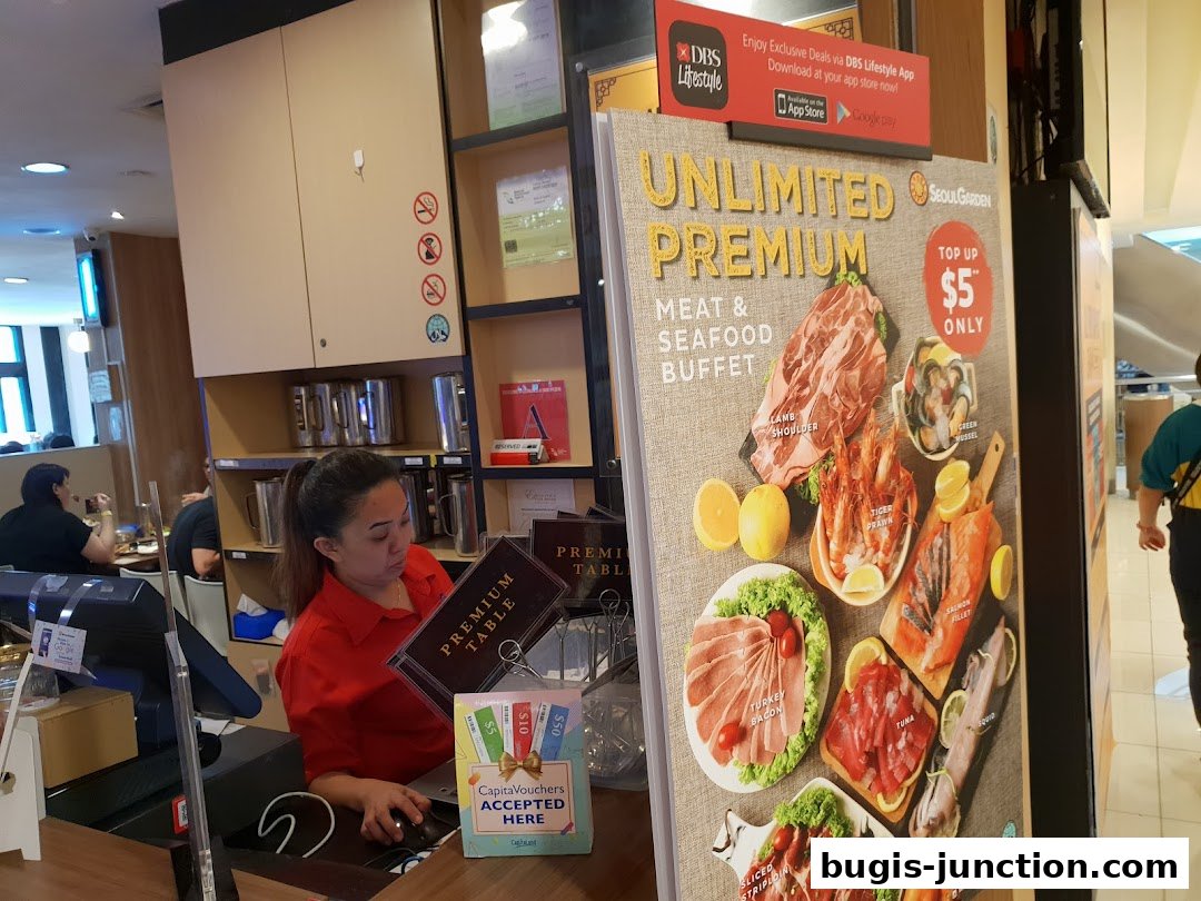 A restaurant counter with a staff member and a promotional poster for a premium meat and seafood buffet.