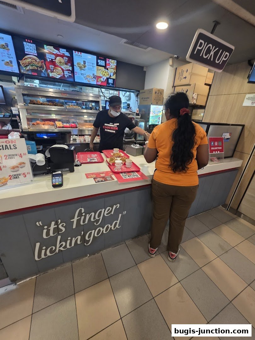 A customer receives food from an employee at a KFC counter with a 'Pick Up' sign.
